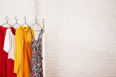 Kadın kalçalı giyim mağazasının iç mekanı. Alışveriş merkezindeki hippi moda şovu odasında askıda asılı renkli kadın kıyafetleri. Beyaz tuğlalı arka plan. Boşluğu kopyala.