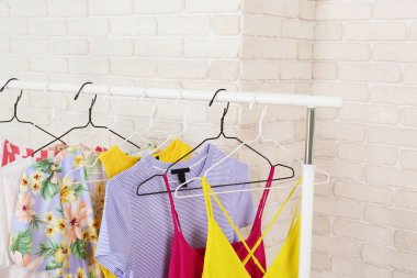 Kadın kalçalı giyim mağazasının iç mekanı. Alışveriş merkezindeki hippi moda şovu odasında askıda asılı renkli kadın kıyafetleri. Beyaz tuğlalı arka plan. Boşluğu kopyala.