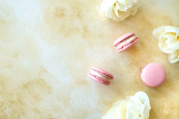 Composición femenina con dulces tradicionales macarrones franceses y tiernas flores de tulipán bicolor sobre fondo texturizado de hormigón amarillo. Vista superior, primer plano, espacio para copiar . —  Fotos de Stock