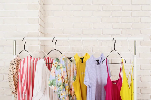 Roupas femininas loja de roupas conceito interior. Fila de roupas femininas coloridas diferentes penduradas no rack na sala de desfile de moda hipster no shopping center. Fundo de parede de tijolo branco. Espaço de cópia . — Fotografia de Stock