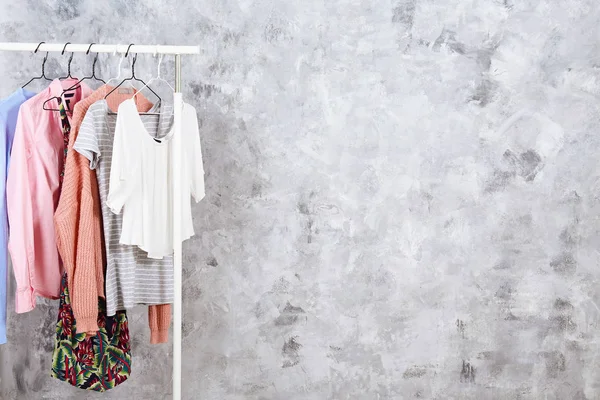 Mujer de moda tienda de ropa concepto interior. Fila de ropa femenina de diferentes colores colgando en rack en la sala de desfiles de moda hipster en el centro comercial. Fondo de pared de hormigón grueso. Copiar espacio . —  Fotos de Stock