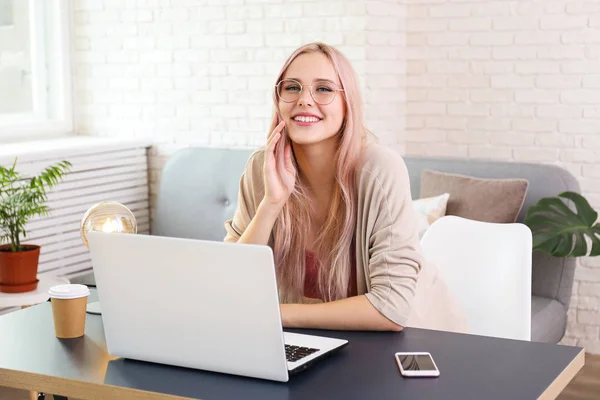 Junge schöne blonde Frau mit rosa Haartoner sitzt an ihrem Arbeitsplatz mit weißem Laptop. Porträt eines weiblichen Teenie-Models im Innenraum eines Eckbüros. Nahaufnahme, Kopierraum, Hintergrund. — Stockfoto