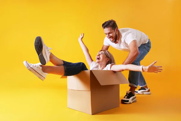 Pareja joven en trajes a juego que se divierten moviendo cajas, aislado en amarillo . — Foto de Stock