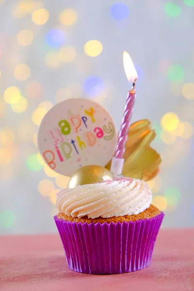 Dulce bizcocho orgánico feliz cumpleaños con vela encendida en envoltura púrpura, crema de queso glaseado remolino y decoración de chocolate dorado en mesa texturizada de madera blanca. Cerrar, copiar espacio, fondo . —  Fotos de Stock