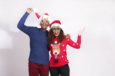 Genç bir çiftin stüdyo portresi, koyu tenli erkek arkadaş ve kız arkadaş Noel Baba şapkası ve Noel Baba kıyafeti giyiyor. Çirkin kazak konsepti. Kapat, metin için boşluk kopyala, izole arkaplan.