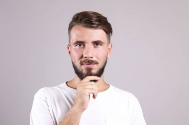 Gri arka planda poz veren mükemmel bakımlı sakallı bir adam..