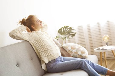 Kıvırcık saçlı esmer kadın evdeki kanepede dinleniyor..