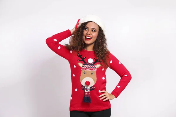 Studio portrait of young woman with dark skin and long curly hair wearing tight santa claus hat and christmas outfit. Ugly sweater concept. Close up, copy space for text, isolated background. — Stock Photo, Image