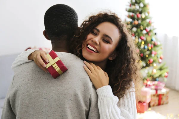 Portrait of young couple, boyfriend & girlfriend with dark skin wearing santa claus hat and christmas outfit exchanging gifts at home. Close up, copy space for text, isolated background.