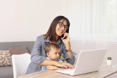 Evinde çocuğuyla çalışan genç bir anne. Fotokopi alanı olan beyaz duvar arkaplanı..