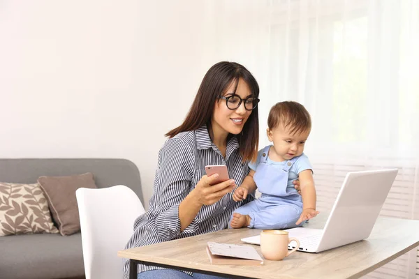 Young mother working at home office with her child, white wall background with copy space.