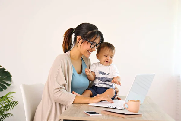 Mladá matka pracuje doma kancelář se svým dítětem, bílá zeď pozadí s kopírovacím prostorem. — Stock fotografie