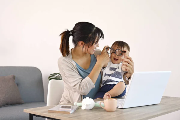 Ung mamma arbetar på hemmakontoret med sitt barn, vit vägg bakgrund med kopieringsutrymme. — Stockfoto