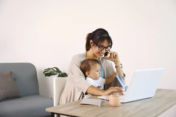 Jeune mère travaillant au bureau à la maison avec son enfant, fond mural blanc avec espace de copie . — Photo