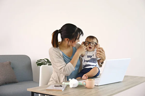 Fiatal anya dolgozik otthon irodában gyermekével, fehér fal háttér fénymásoló hely. — Stock Fotó