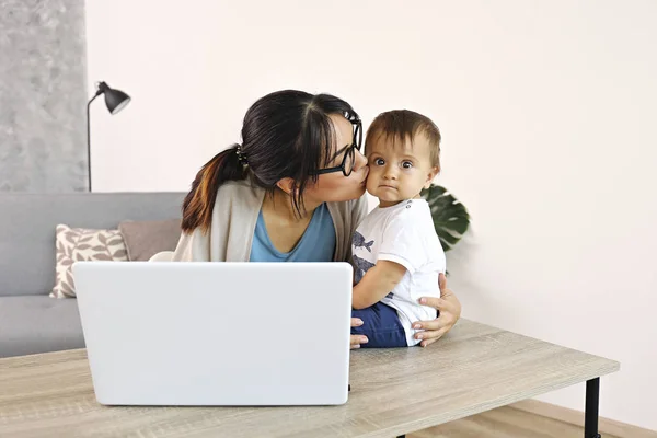 Ung mamma arbetar på hemmakontoret med sitt barn, vit vägg bakgrund med kopieringsutrymme. — Stockfoto