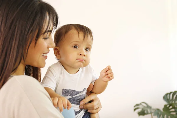 Portrét mladé matky, jak se doma stará o svého malého syna. Krásná fena s rovnými brunetkami vlasy hrát s dítětem v obývacím pokoji. Zavřít, kopírovat prostor, pozadí. — Stock fotografie