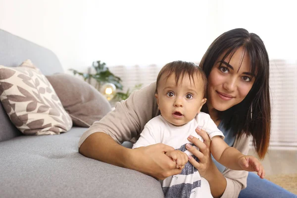 Portrét mladé matky, jak se doma stará o svého malého syna. Krásná fena s rovnými brunetkami vlasy hrát s dítětem v obývacím pokoji. Zavřít, kopírovat prostor, pozadí. — Stock fotografie