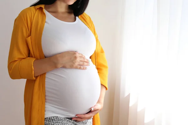 Jonge vrouw houdt haar zwangere buik op de negende maand van de zwangerschap. — Stockfoto