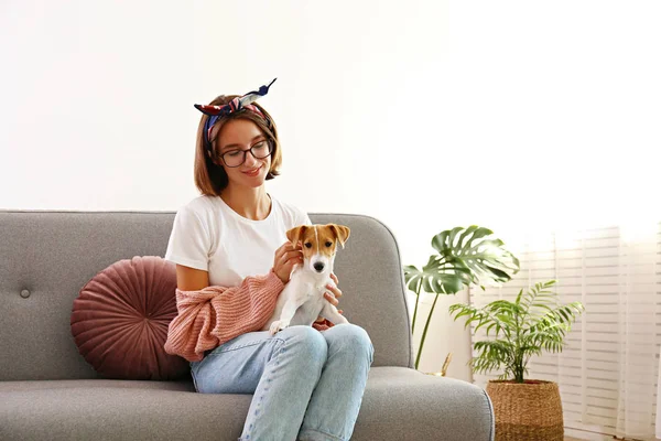 Retrato de una joven mujer hipster hermosa con su adorable cachorro Jack Russell terrier de cuatro meses de edad en casa en la sala de estar llena de luz natural del sol. Fondo interior elevado, primer plano, espacio para copiar . — Foto de Stock