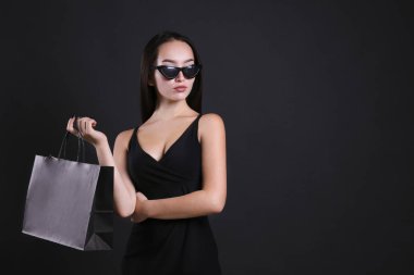 Siyah giyinmiş, alışveriş çantasıyla poz veren genç bir kadın..