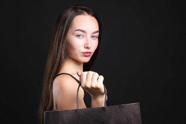 Siyah giyinmiş, alışveriş çantasıyla poz veren genç bir kadın..