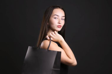 Siyah giyinmiş, alışveriş çantasıyla poz veren genç bir kadın..