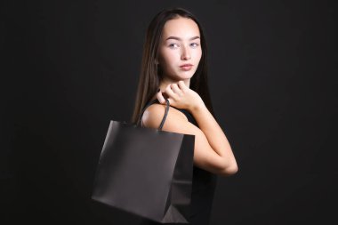 Siyah giyinmiş, alışveriş çantasıyla poz veren genç bir kadın..