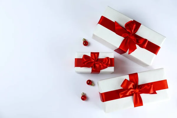 光沢のある絹の弓で結ばれた赤と白の紙に包まれたクリスマスプレゼントの束。赤と白の包装で複数の新しい年の贈り物。トップビュー、閉じる、コピースペース、背景、フラットレイアウト. — ストック写真