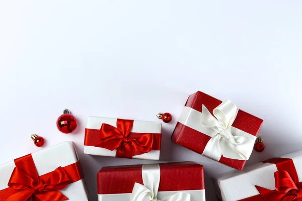 光沢のある絹の弓で結ばれた赤と白の紙に包まれたクリスマスプレゼントの束。赤と白の包装で複数の新しい年の贈り物。トップビュー、閉じる、コピースペース、背景、フラットレイアウト. — ストック写真