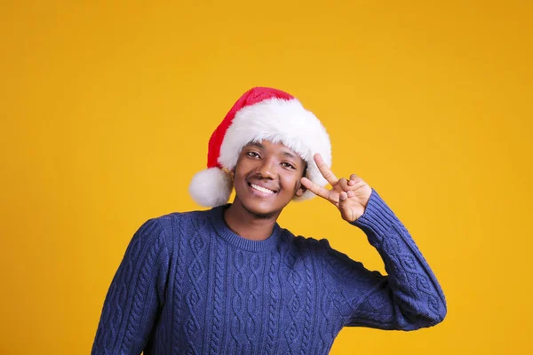 Hombre afroamericano con elegante camisa a cuadros gran sonrisa en sombrero de santa con caja de regalo en fondo amarillo studio.dark-skin Santa Claus felicitando feliz Navidad — Foto de Stock