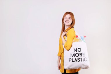 Duygusal kızıl saçlı kadın artık plastik metin, zararlı ürünler, şişe ve çanta dolu çevre dostu alışveriş çantası tutan. Sıfır atık kavramı. Mutlu kadın sıralama, garabage ayıran.