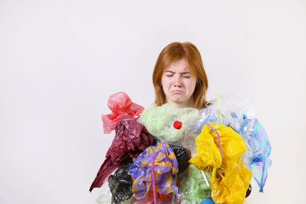 Emotionell rödhårig kvinna ser stressad, täckt med Eco skadliga plast sopor, väskor och strån av olika färg. Inget avfalls koncept. Ledsen kvinnlig rynkning, arg på nedskräpning. — Stockfoto