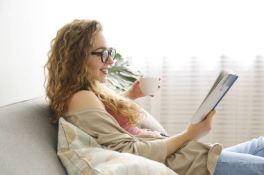 Kıvırcık saçlı esmer kadın evdeki kanepede dinleniyor..