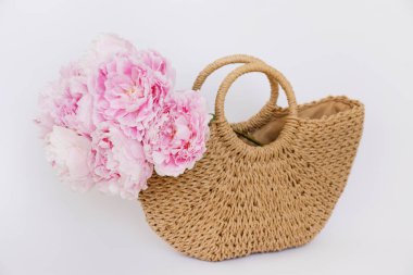 Bahar çiçekleriyle süslü bir hasır çantanın kavramsal görüntüsü. Beyaz arka planda pembe şakayık desenli bir kadın. Kapat, kopyala boşluk, kırpılmış çekim.