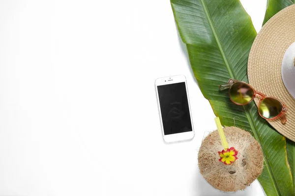 Summer mood concept. Fresh whole coconut w/ straw, mirrored sunglasses, broad brim hat, blank screen phone on banana palm leaves. Flat lay, top view, close up copy space, isolated, tropical background