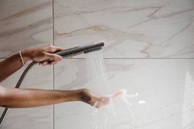 Genç bir kadının duş başlığını tutarken mermer desenli banyonun duvarında akan suyla çekilmiş bir fotoğrafı. Kapat, kopyala boşluk, arkaplan.