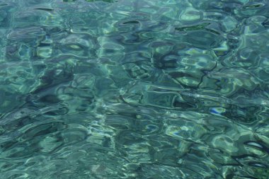 Turkuaz okyanus suyunun ışık yansıma dokusuyla yakın çekimi. Açık deniz, parlak güneş desenleri ve görünür kıçı. Tropik arka plan konsepti. Kapat, metin için boşluk kopyala.