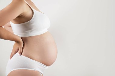 Destekleyici, kusursuz annelik sütyeni ve maksimum altı olan hamile bir kadın. Kocaman, çıplak karnına sarılmış kadın elleri. Çocuk beklentisi konsepti. Arkaplan, boşluğu kopyala