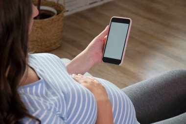Hamileliğinin üçüncü üç ayında telefonunu kullanan güzel bir kadın. Boş ekran akıllı telefonuyla hamile bir kadını kapat. Çocuk konsepti bekliyorum. Arkaplan, boşluğu kopyala.