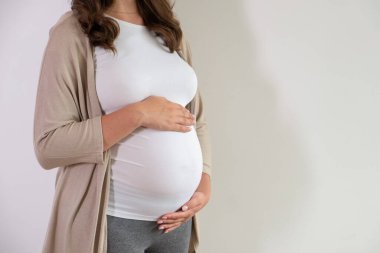 Hamileliğin üçüncü üç ayında güzel bir kadının portresi. Kollarını karnına dayamış hamile bir kadına yaklaş. Çocuk konsepti bekliyorum. Arkaplan, boşluğu kopyala.