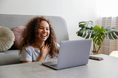 Laptop bilgisayarını kullanan esmer ve uzun kıvırcık saçlı genç bir kadının portresi. Afrika kökenli Amerikalı kadın görüntülü arama. Merkez ofisteki serbest çalışan. Kapat, kopyala boşluk, arkaplan.