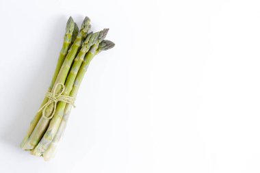 Beyaz arka planda bir sürü çiğ kuşkonmaz sapı var. Yenebilir kuşkonmaz resmi filizleri pamuk sicimle bağlanmış. Kapat, boşluğu kopyala, üst görünüm, düz yatış.