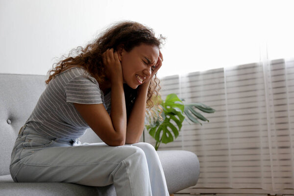 Портрет молодой красивой черной женщины, испытывающей мучительную мигрень, хватающую ее за голову. Женщина выражает физическую и эмоциональную боль. Грустная девушка в своей комнате. Фон, копировальное пространство.