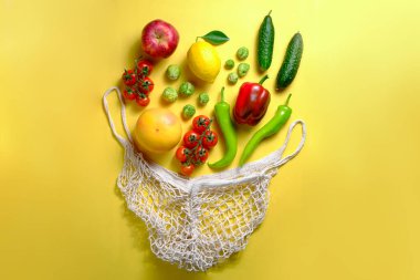 Yeniden kullanılabilir pamuk iplik torbasında bir sürü karışık organik meyve, sebze ve yeşillik. Sıfır atık. Vegan 'ın market çantası Sarı arkaplan, kopyalama alanı, kapalı, izole edilmiş.