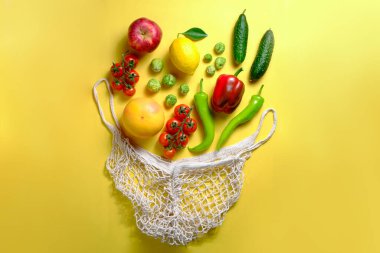 Bunch of mixed organic fruit, vegetables & greens in reusable cotton string net bag. Zero waste concept. Vegan's grocery bag Yellow background, copy space, close up, isolated. clipart