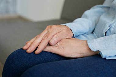 Yaşlı bir kadın evde tek başına oturuyor, elleri kucağında. Yaşlı bir kadın şiddetli romatizma ağrıları çekiyor, masaj yapıyor, kollarını ısıtıyor. Kapat, kopyala boşluk, arkaplan