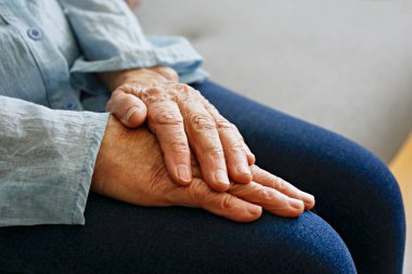 Yaşlı bir kadın evde tek başına oturuyor, elleri kucağında. Yaşlı bir kadın şiddetli romatizma ağrıları çekiyor, masaj yapıyor, kollarını ısıtıyor. Kapat, kopyala boşluk, arkaplan