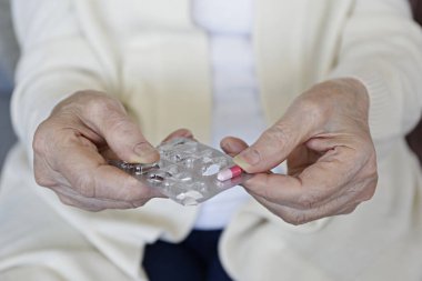 Üst düzey bir bayan son bir hapla su toplamış. Tek kapsüllü bej hırka ve kot pantolon giyen yaşlı bir kadın. Kapat, kopyala boşluk, arkaplan.