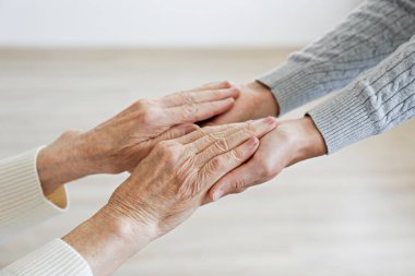 Büyükannesi evde torunundan yardım alıyor. Yaşlı bir bayanın genç bir kadınla el ele tutuşurken yakın plan çekimleri. Boşluğu kopyala, arkaplan.